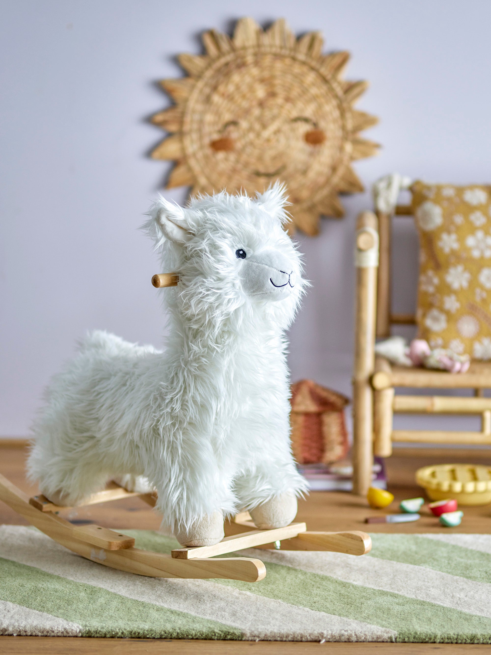 Plush rocking toy shaped as a llama with white, fluffy fur. Placed in a children's room with purple walls on a white and green carpet. 