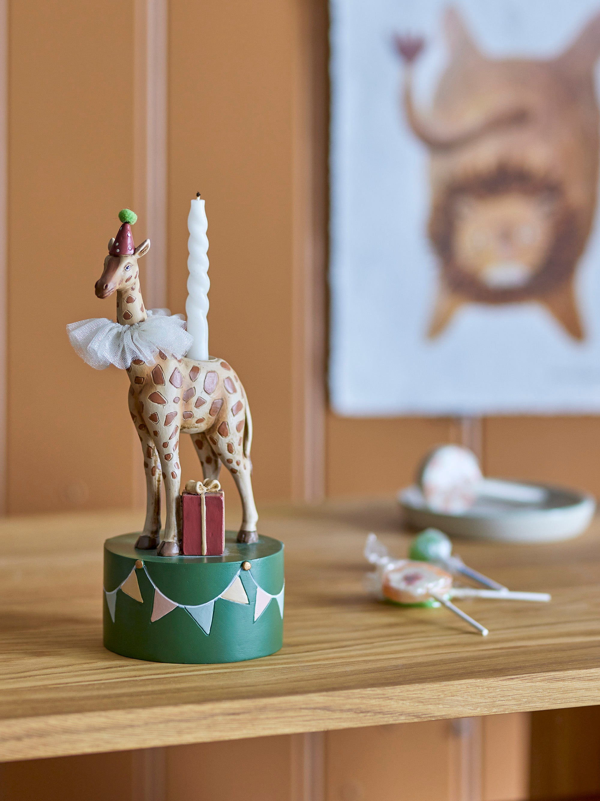 A birthday-themed candleholder, shaped as a giraffe with a birthday hat, standing on a green podium 