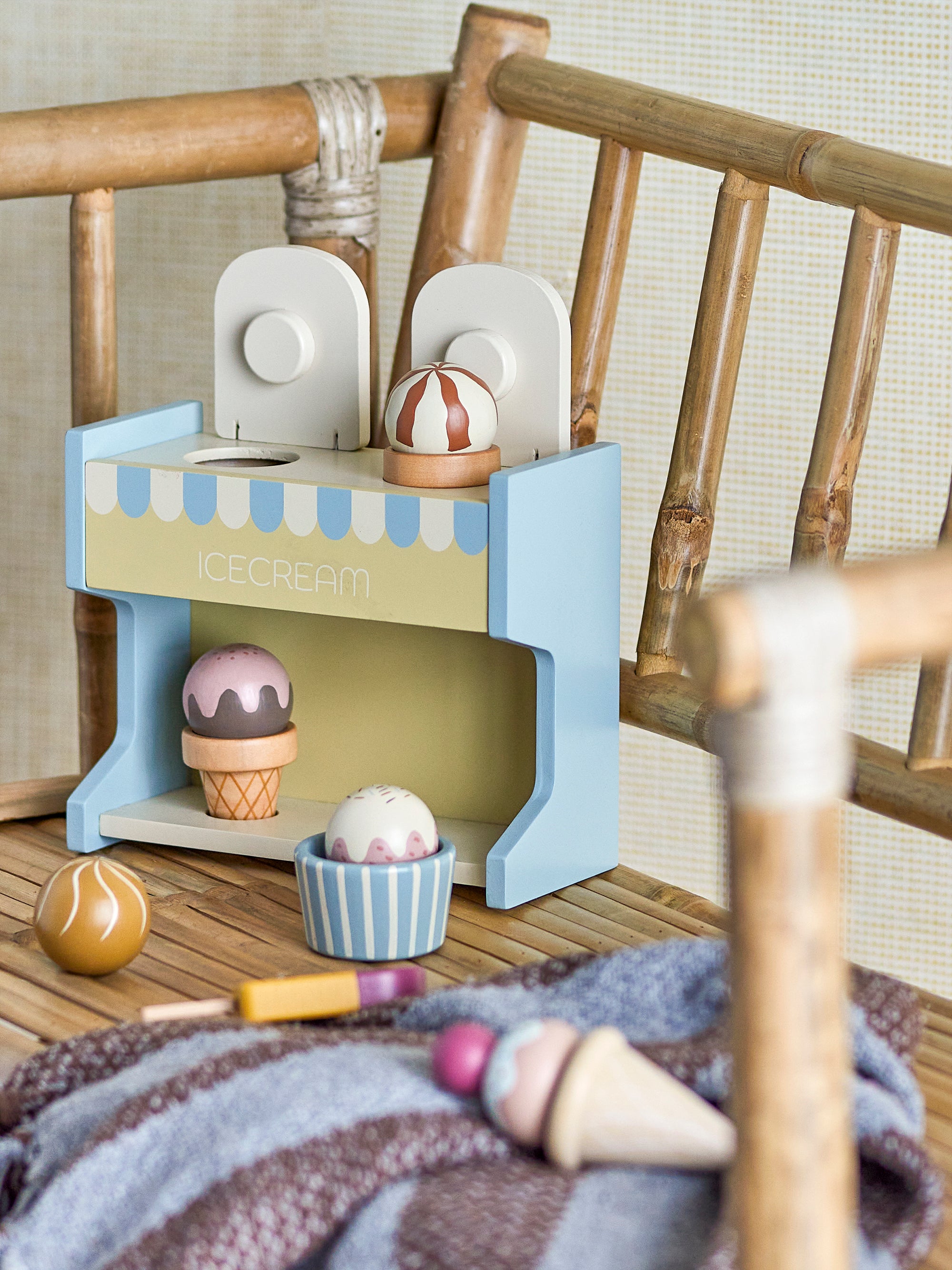 Colorful wooden ice cream toys for children in green, blue and pink, placed in an ice cream stand on a chair. 