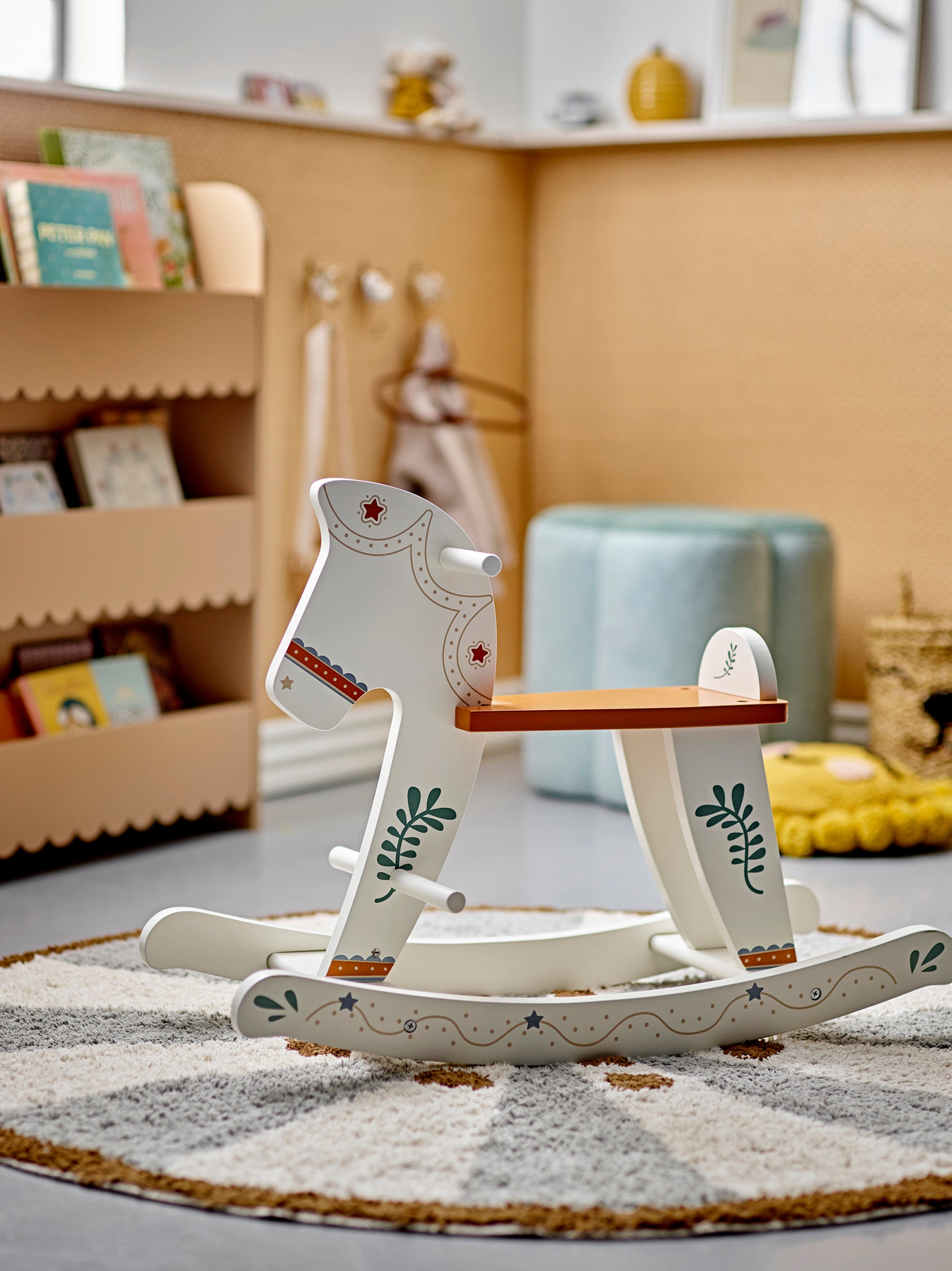 Wooden rocking toy shaped as a horse with a beautiful pattern in green and red. The seat is brown. The horse is placed in a children's room on a round rug. 