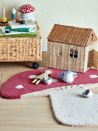 Little rug shaped and colored as a mushroom, with a rattan doll house and a doll placed on it.